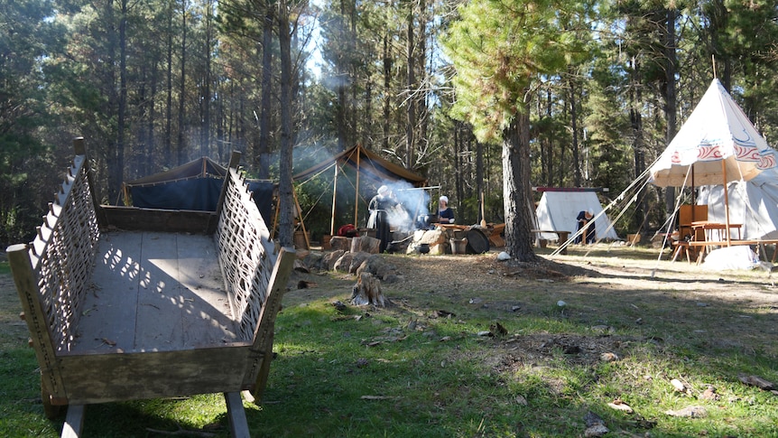 A wicker buggy sits in the foreground of an old fashioned camp site.