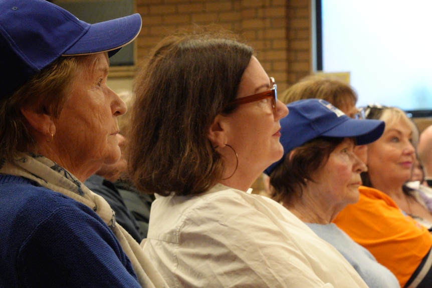 Older women in seats at an event in a community hall.