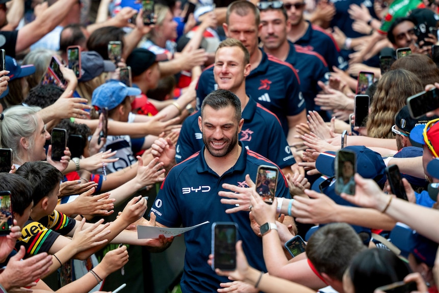 A man leads a rugby league team through a group of fans 