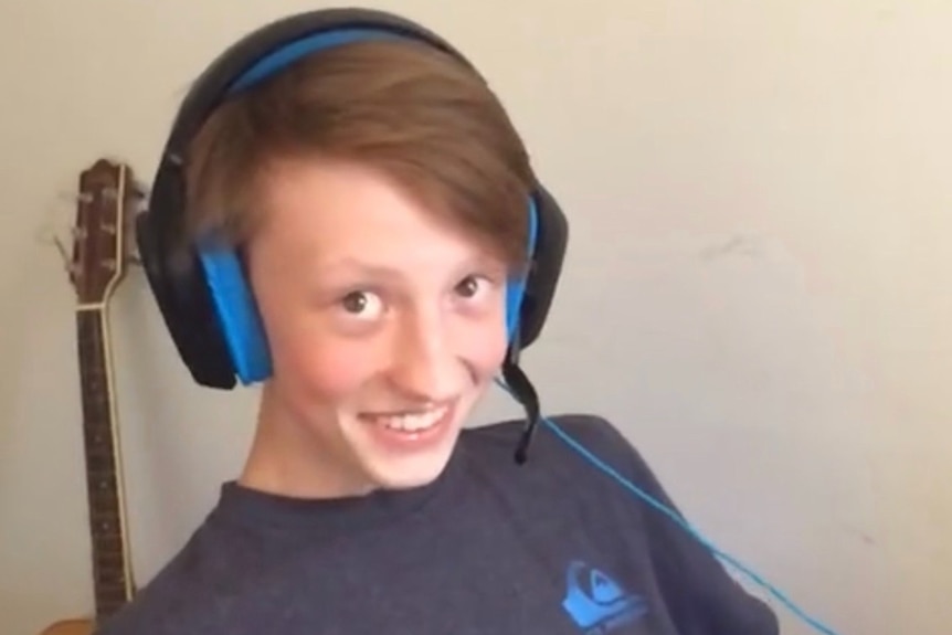A boy in a blue tshirt with wired headphones smiles