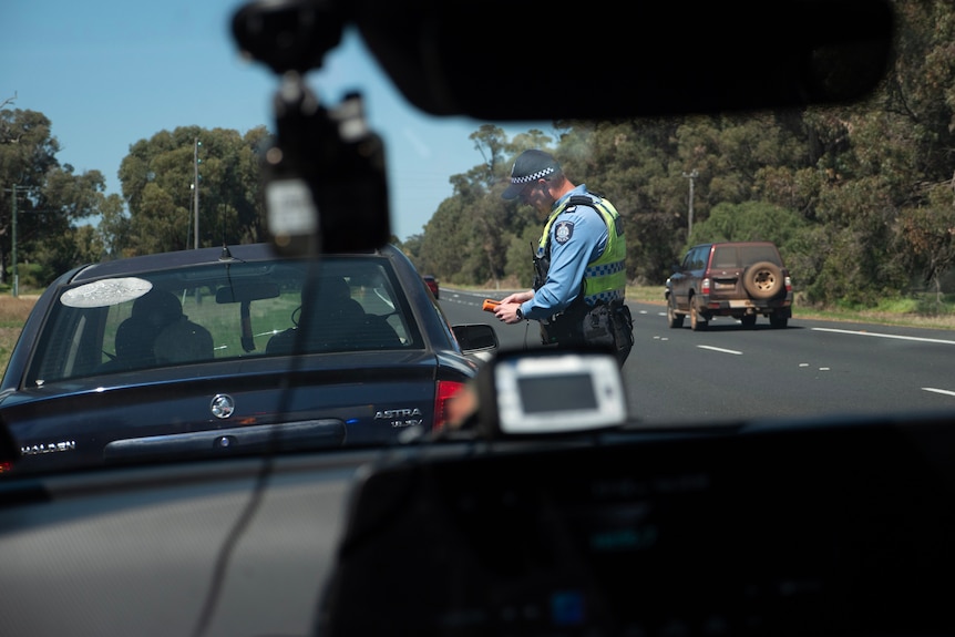 View through front car window of cop breath testing person in their car on side of road