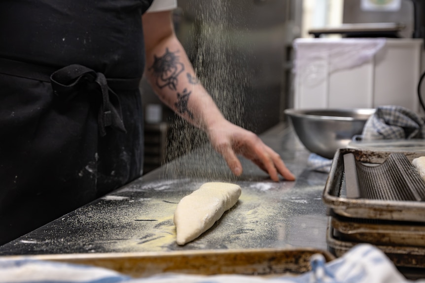 Hands making a baguette with flour sprinkling on top of the dough