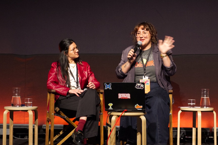 Two people sitting on directors chairs on a stage with microphones
