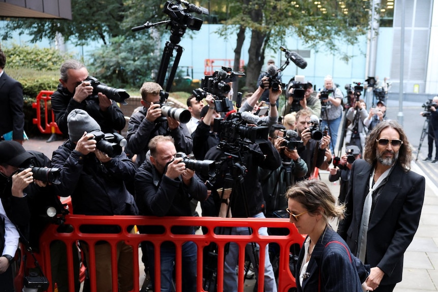 A man and a woman in formal clothing, walking in front of a lot of photographers.