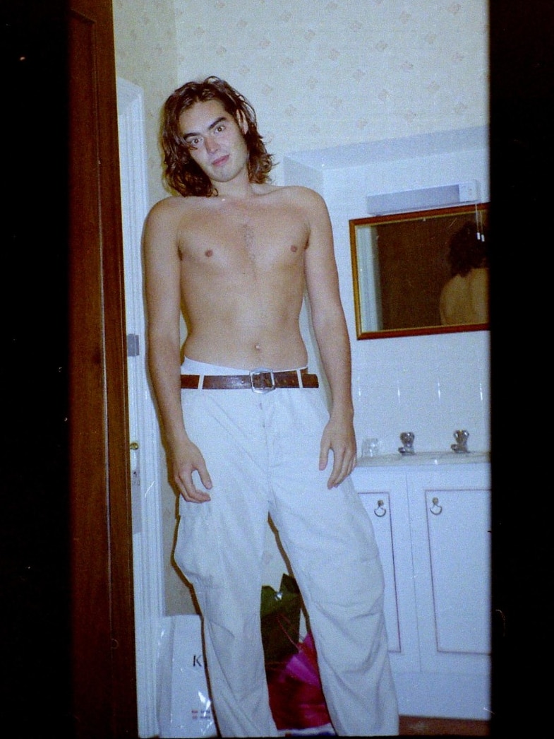 A man wearing trousers and no shirt blowing a kiss at the camera.
