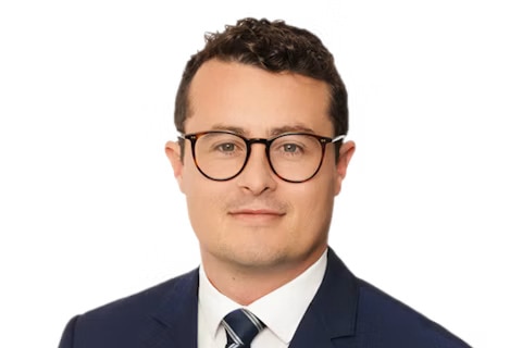 Headshot of a dark-haired man (Sean Sweeney) in a suit and wearing glasses.