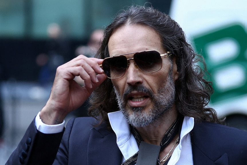 A close-up photo of a man with shoulder length brown hair wearing sunglasses.