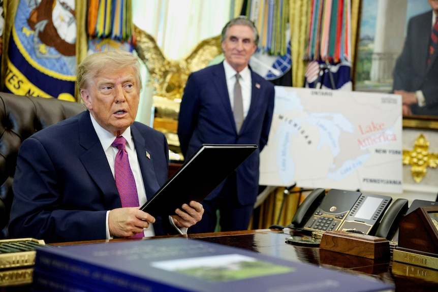 Donald Trump holds a black folder with a map of the renamed Lake America in the background.