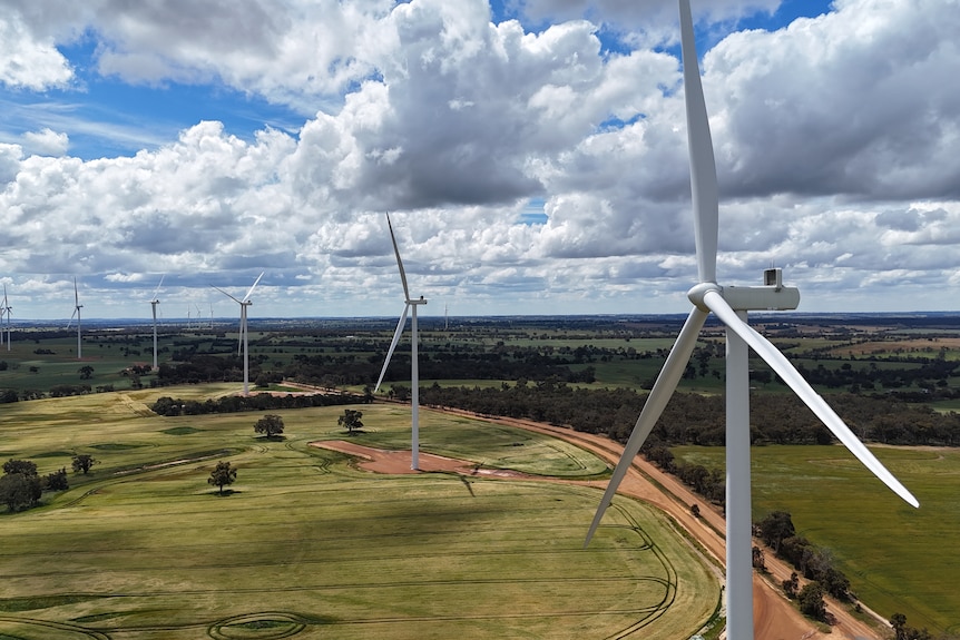 Aerial shot of a row of wind turbines in green farmland under a cloud-speckled sky