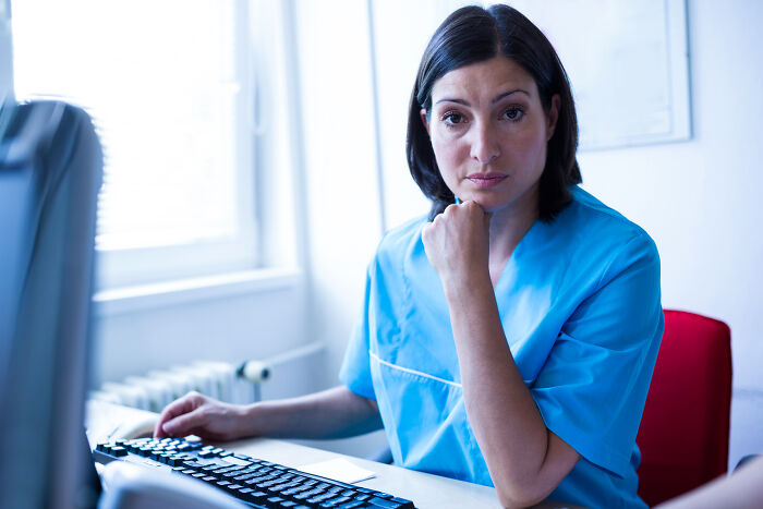 A healthcare worker wearing blue scrubs looking at a computer screen.