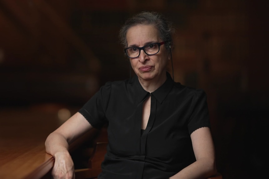 A woman sits in a chair as she is interviewed for television.