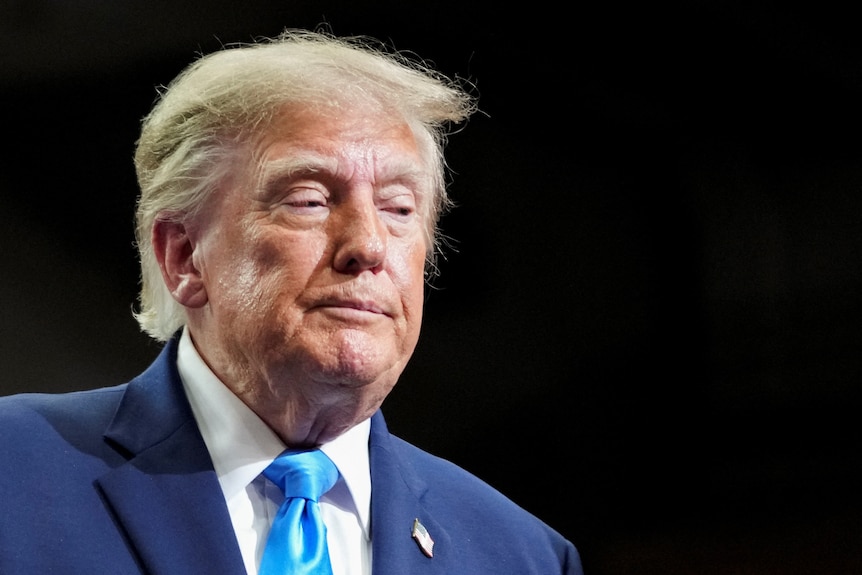 Donald Trump wears a blue suit and tie with a forlorn look on his face.