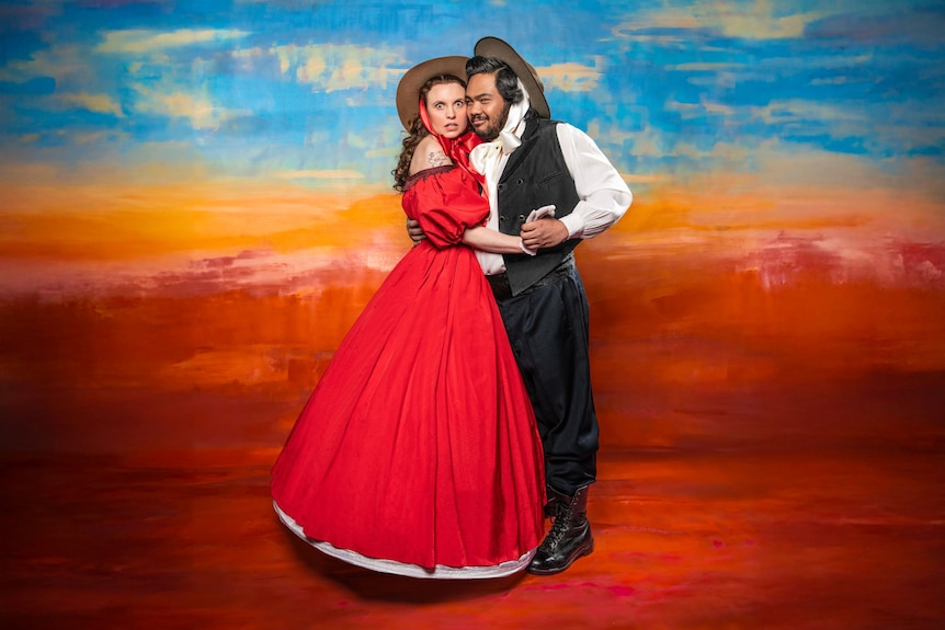 John Marc Desengano, Filipino Australian, with a sly expression, holds a scared-looking Elizabeth Brennan, in a red gown, close.