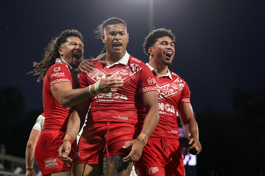 Three rugby league players in red celebrate a try to the camera