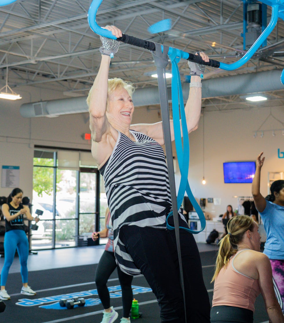 A diverse group of women engaged in a fitness class, with one woman performing a pull-up on gym equipment.