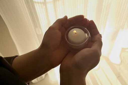 Two hands holding a small white candle