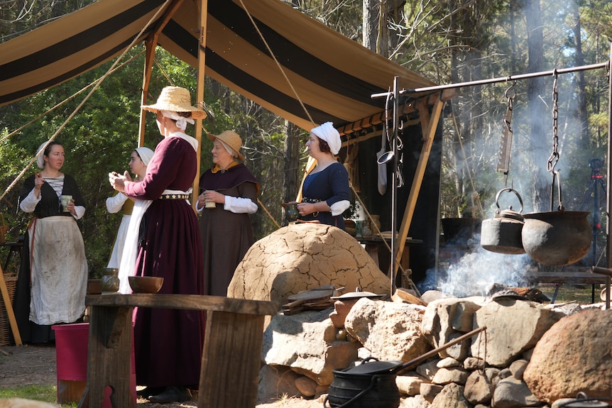 A group of women in middle high ages clothing gather around a camp fire