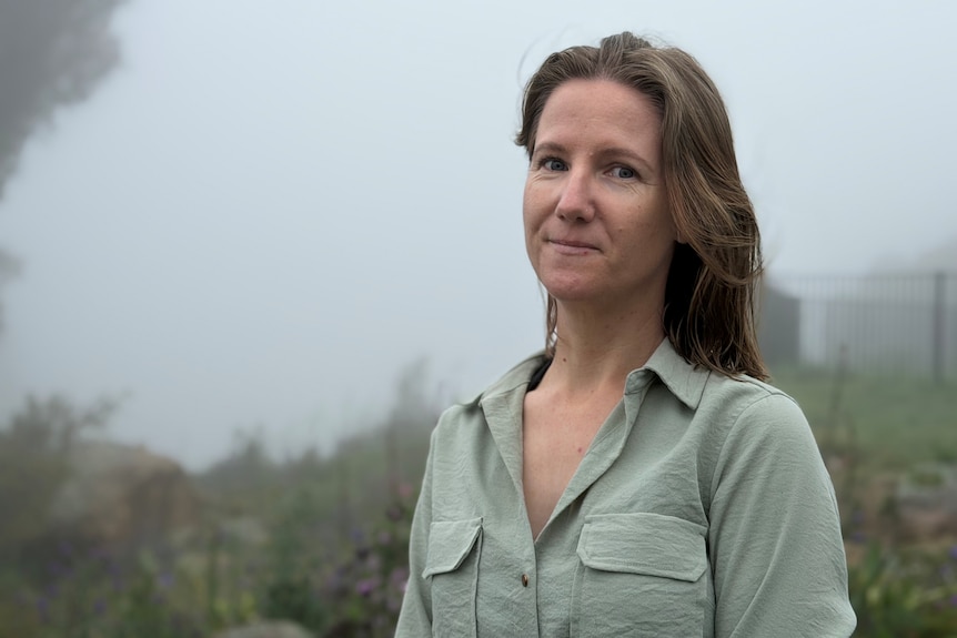 A woman in a green shirt stands in a garden shrouded in mist. 