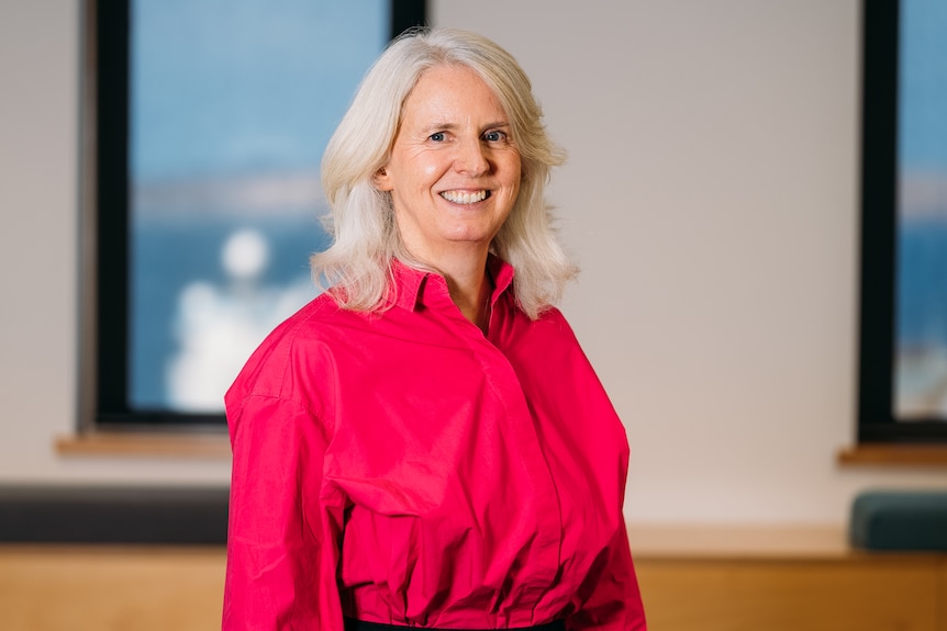 a blonde woman wearing a pink shirt smiling at the camera