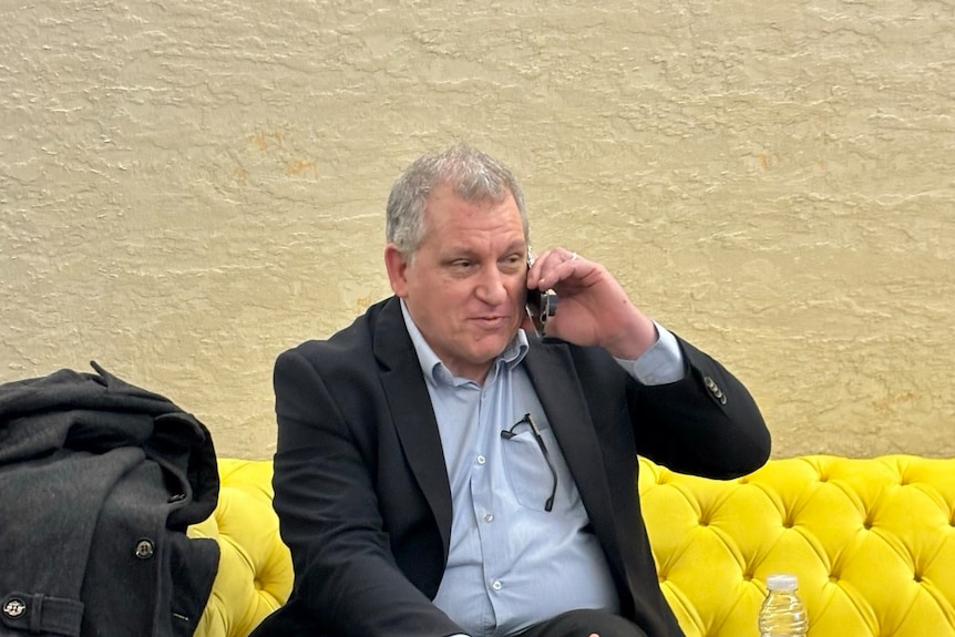 Robert Pether sitting on yellow couch and speaking on phone.