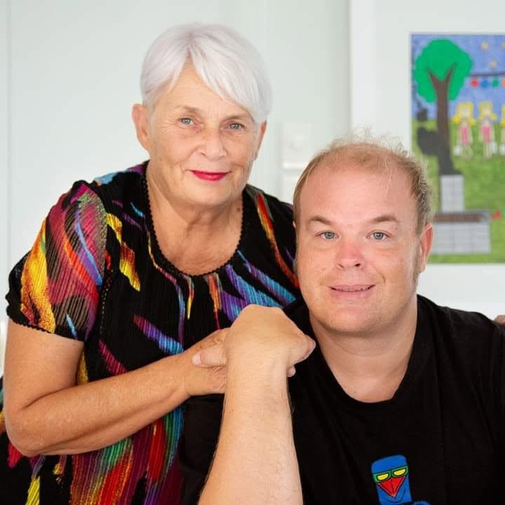 An older woman standing next to her son on a balcony both smiling for the camera