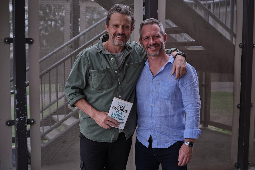 David, left, and Tim smile with arms wrapped loosely around each other as they pose for a photo.