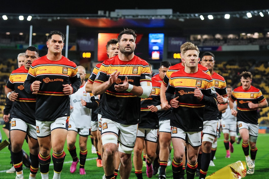 A team runs out onto a field in jerseys and shorts.