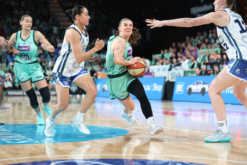 Stephanie Reid holds the ball as opposing players stretch out warding hands.
