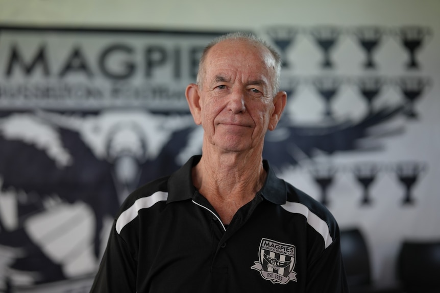 A man in a black and white polo shirt standing in front of a magpie mural on a wall