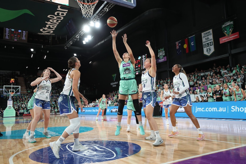 Darcee Garbin shoots with the ball as other crowd around her near the basketball hoop.