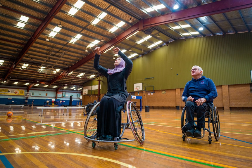 Reema El Qassem throws a basketball at the hoop while her coach looks on behind her.