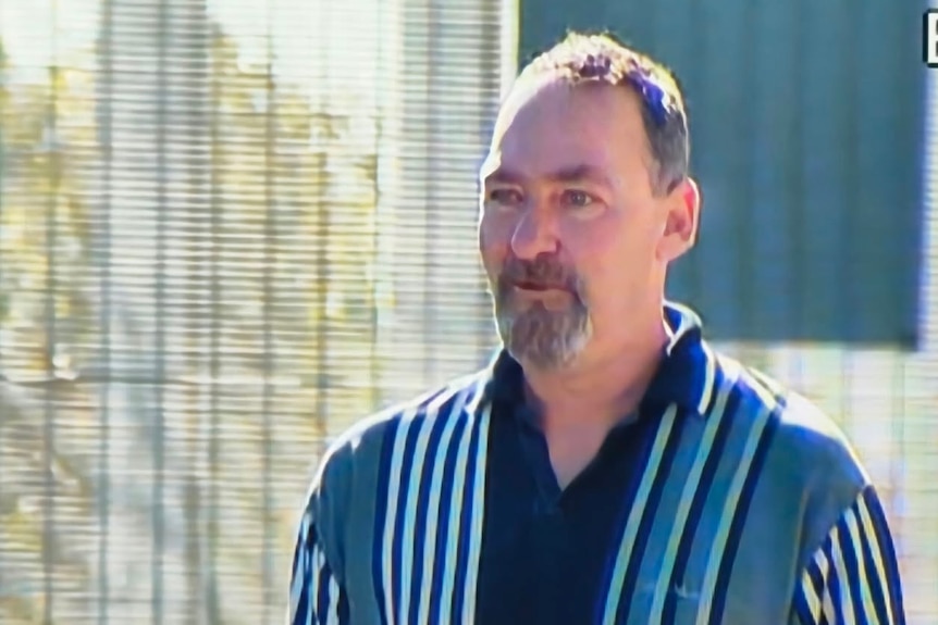 A man in a stripe polo short walks past a fence