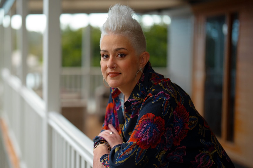 Katie Noonan with short, styled platinum hair leans over a white vernadah banister.
