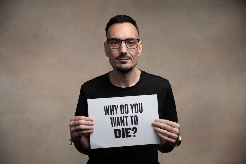 A man holds up a piece of paper with the question "why do you want to die?" on it.