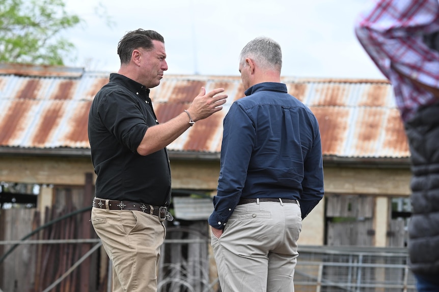 two men talking in front of shed