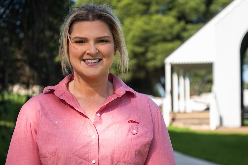 A woman in a pink shirt standing and smiling in a park