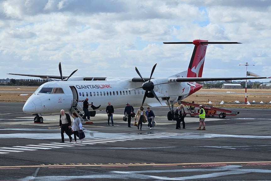 A small plane with a qantas logo and passengers departing onto the tarmac