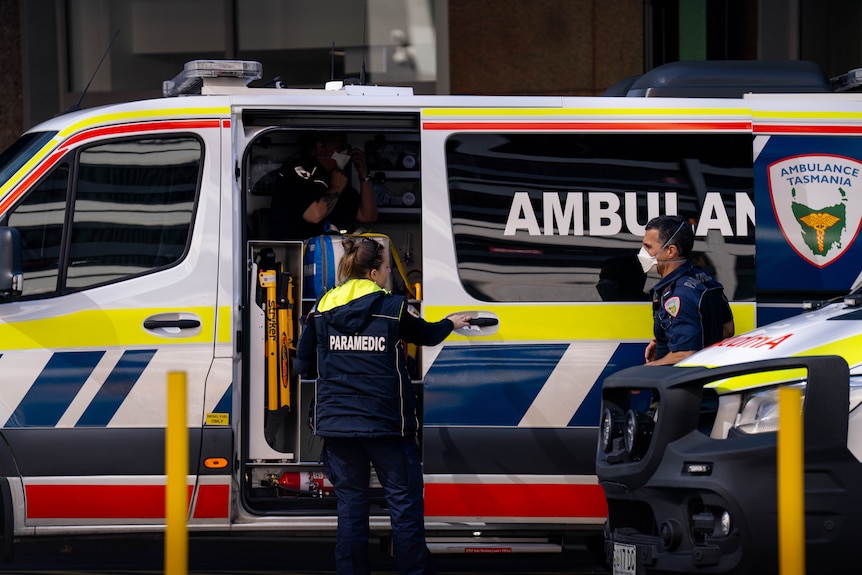 A paramedic opening an ambulance, standing beside another emergency services worker wearing a face mask.