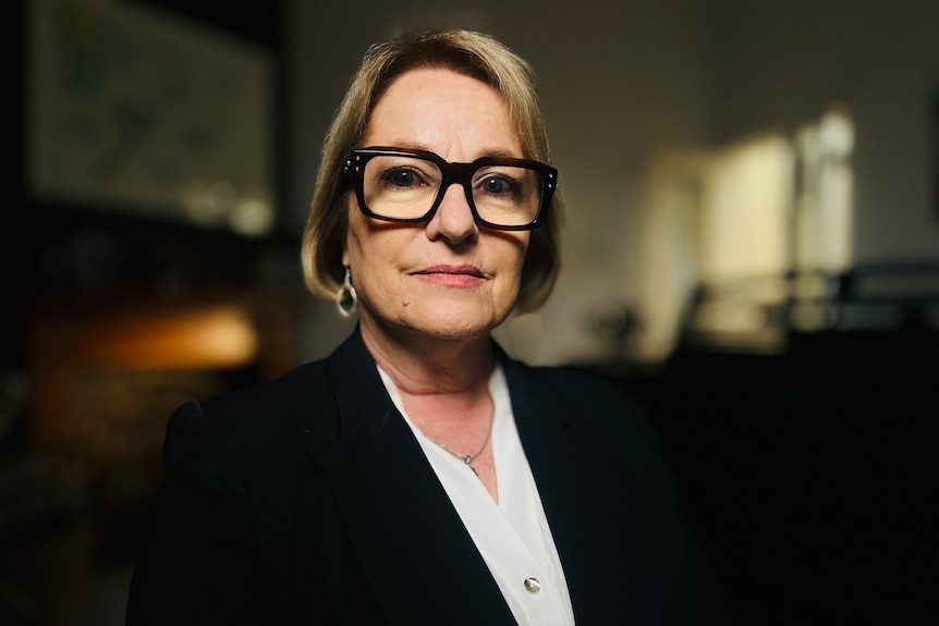 a middle-aged professional-looking woman wearing a dark blazer and reading glasses