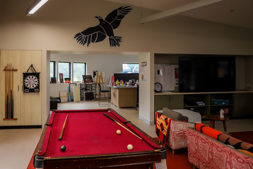 A wide room with a pool table in the centre, with couches adjoining and an art room in the background