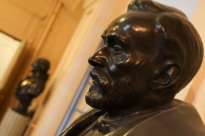 A bronze bust of Alfred Nobel is displayed in a brightly lit room.