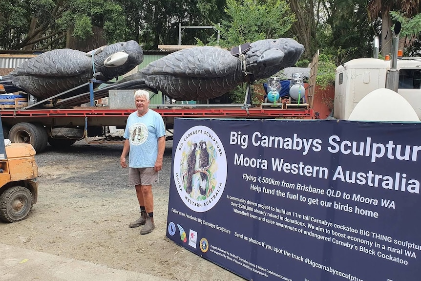 A man stands in front of a truck and trailer carrying two giant black cockatoo sculptures.