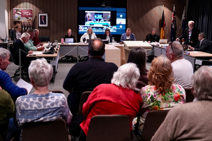 People sit in rows facing a group of people seated at tables for the meeting.