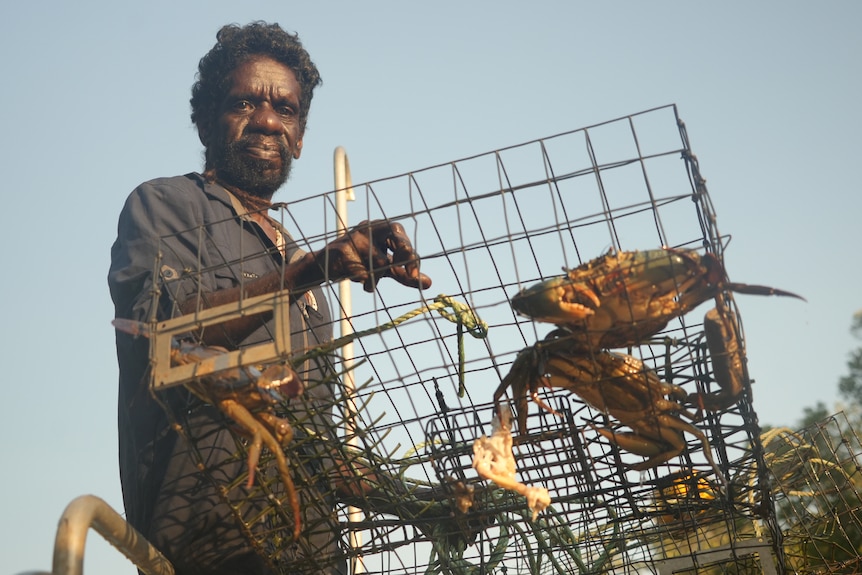 An Indigenous man holding a cage with mud crabs inside.