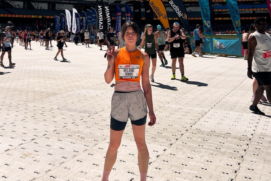 A young woman in running clothes poses with a medal in Federation Square, Melbourne.