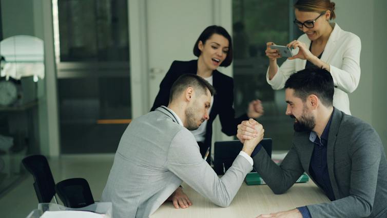 Two men arm-wrestling in the office in front of colleagues