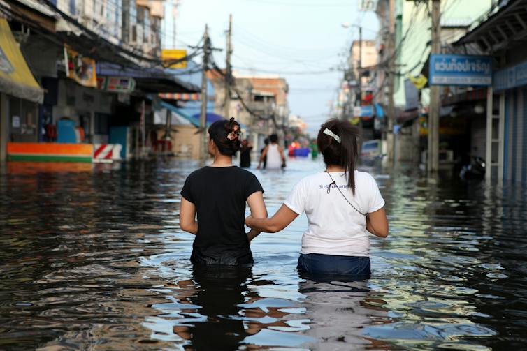 Two friends lock arms as they wade through a flooded street in Bangkok, Thailand.