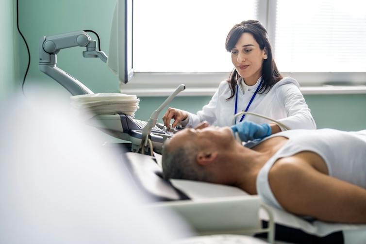 Patient lying on exam table as ultrasound technician places instrument on their neck