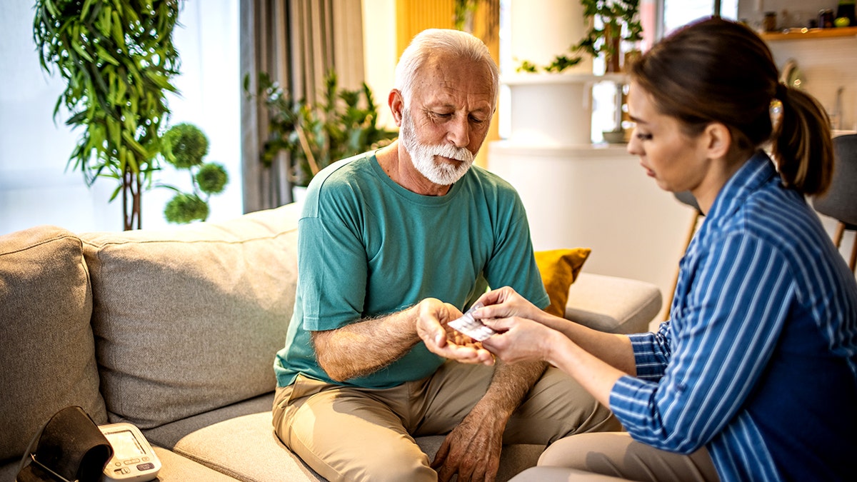 Photo of young woman spending time with her old father, give him some medicine at home