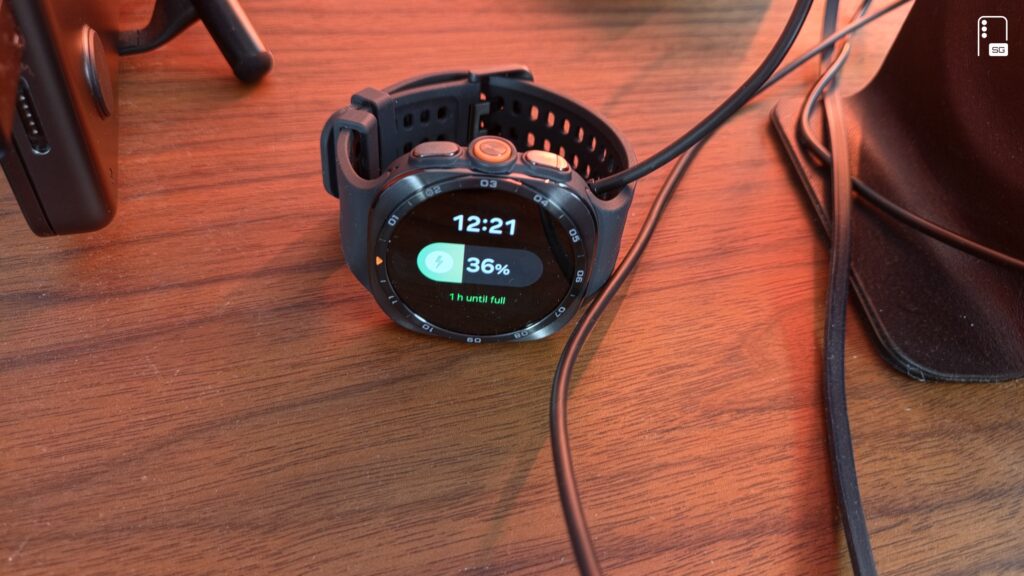 Galaxy Watch Ultra 2 charging on a wooden desk, screen showing 36 percent and one hour until full